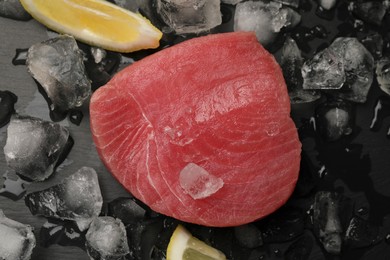 Raw tuna fillet and ice cubes on black table, top view