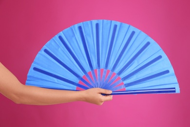 Woman holding blue hand fan on pink background, closeup