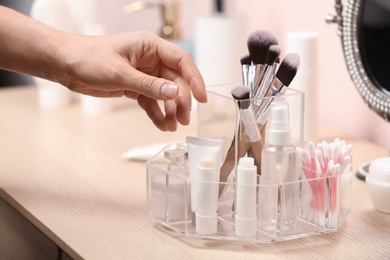 Photo of Woman taking cosmetic products from holder on dressing table, closeup