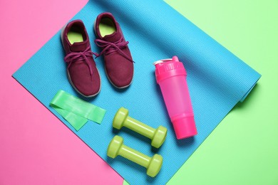 Photo of Exercise mat, dumbbells, fitness elastic band, shoes and shaker on color background, top view