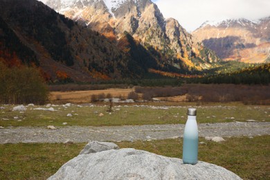 Photo of Thermo bottle on rock in mountains. Space for text