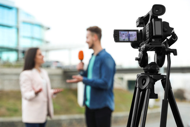 Photo of Young journalist interviewing businesswoman on city street, focus on camera display