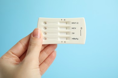 Woman holding disposable express test for hepatitis on light blue background, closeup