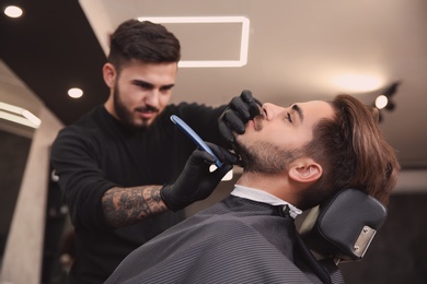 Professional hairdresser shaving client with straight razor in barbershop