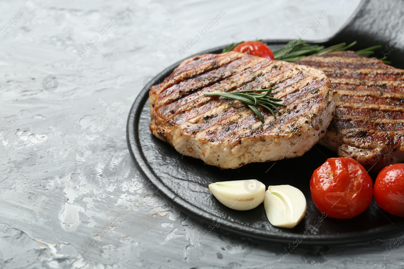 Photo of Delicious grilled pork steaks with spices on gray textured table, closeup. Space for text