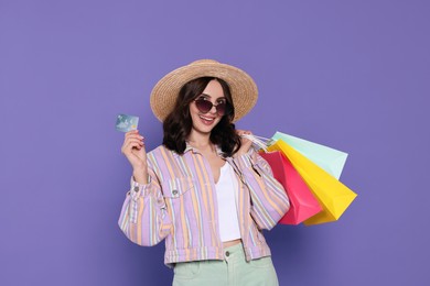 Photo of Beautiful young woman with paper shopping bags and credit card on purple background
