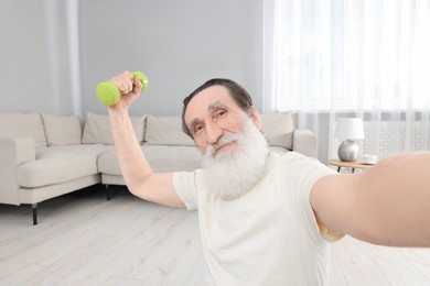 Photo of Senior man taking selfie while exercising with dumbbell at home. Sports equipment