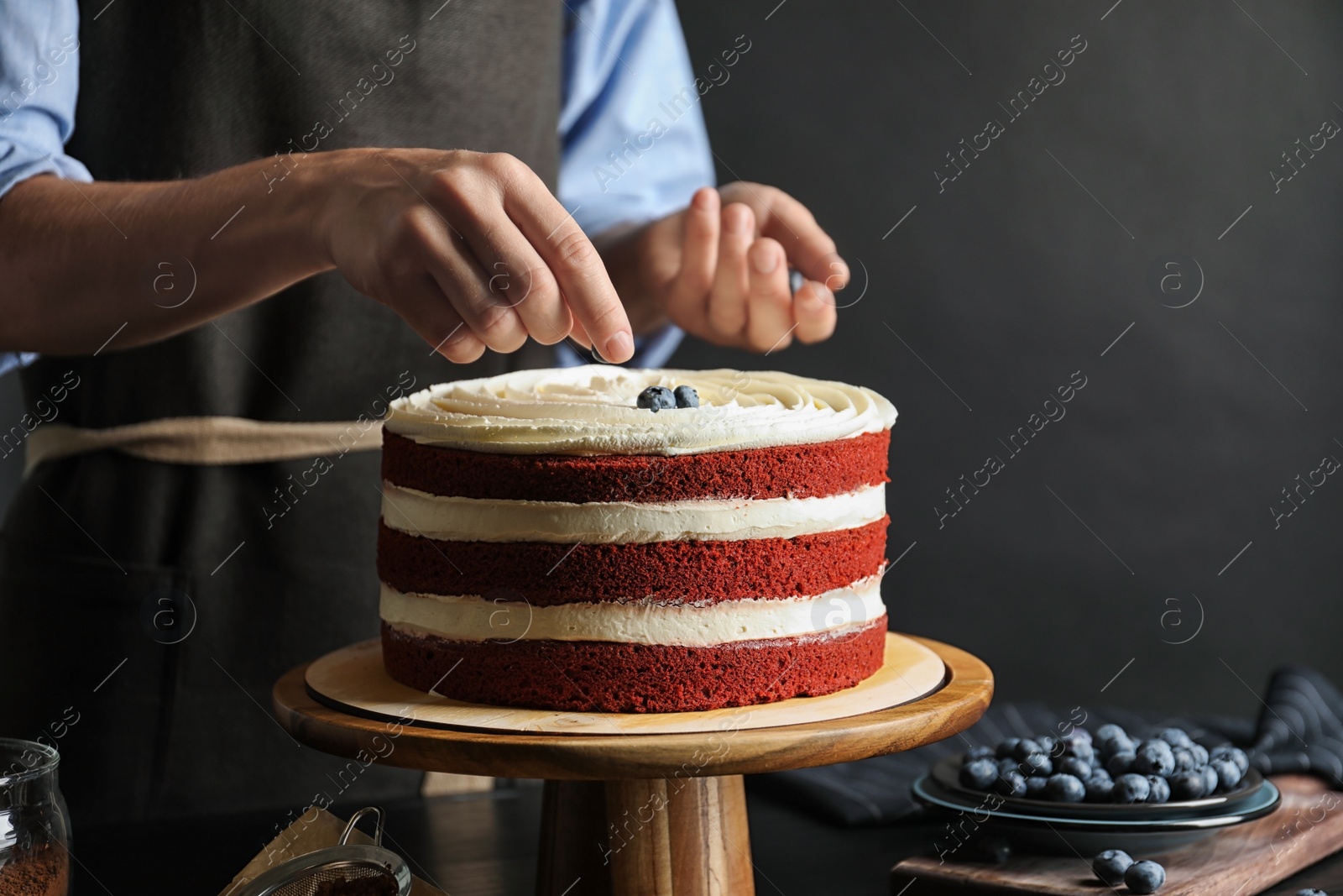 Photo of Woman decorating delicious homemade red velvet cake with blueberries at table