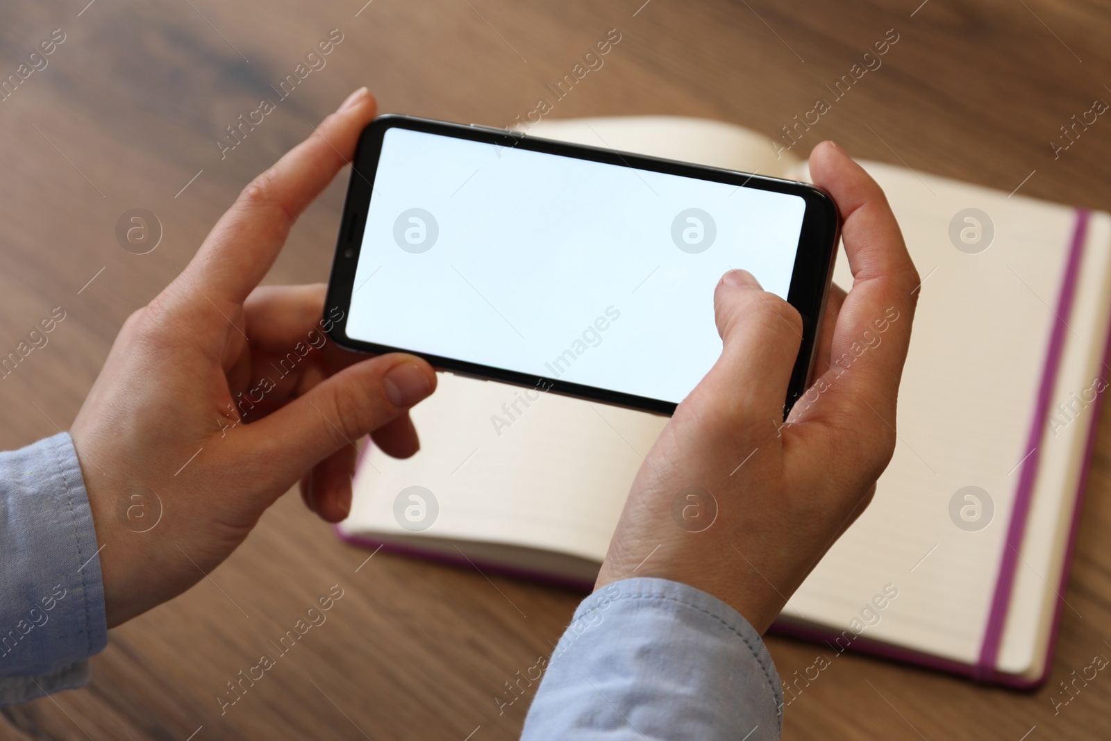 Photo of Woman using smartphone with blank screen at wooden table, closeup. Space for text