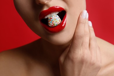 Closeup view of woman with beautiful lips eating candy on red background