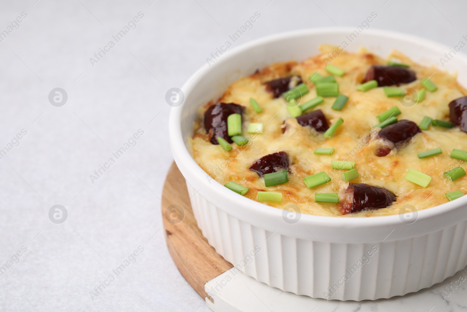 Photo of Tasty sausage casserole with green onions in baking dish on white table, closeup. Space for text