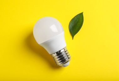 Photo of Light bulb and green leaf on yellow background, flat lay