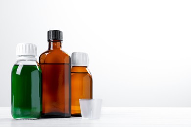 Photo of Bottles of syrups with measuring cup on wooden table against white background, space for text. Cough and cold medicine