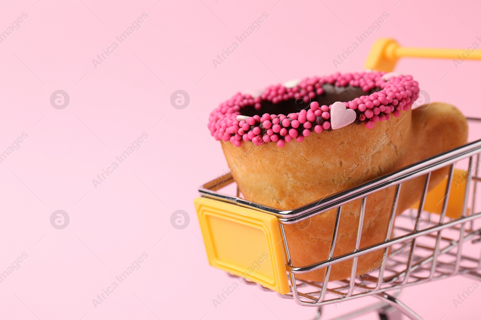 Photo of Delicious edible biscuit coffee cup decorated with sprinkles in shopping cart on pink background, closeup. Space for text