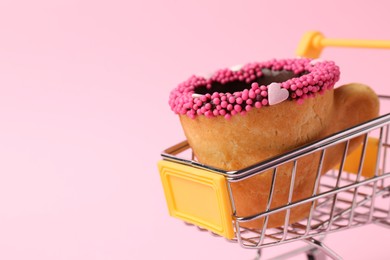 Photo of Delicious edible biscuit coffee cup decorated with sprinkles in shopping cart on pink background, closeup. Space for text