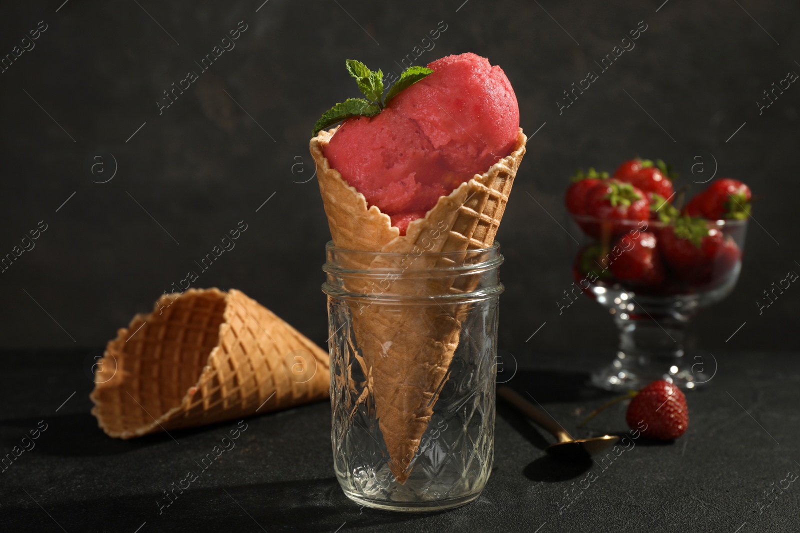 Photo of Delicious strawberry ice cream in wafer cone served on black table