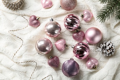 Beautiful pink Christmas baubles on white knitted plaid, flat lay
