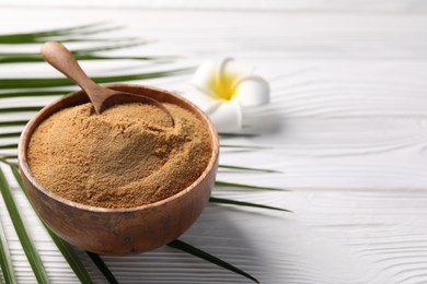 Photo of Coconut sugar and spoon in bowl on white wooden table, closeup. Space for text