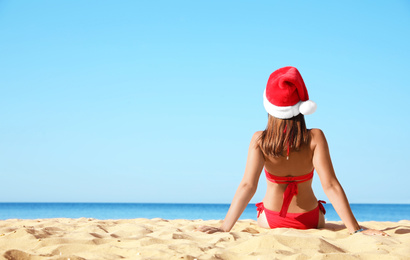 Young woman wearing Santa hat and bikini on beach, space for text. Christmas vacation