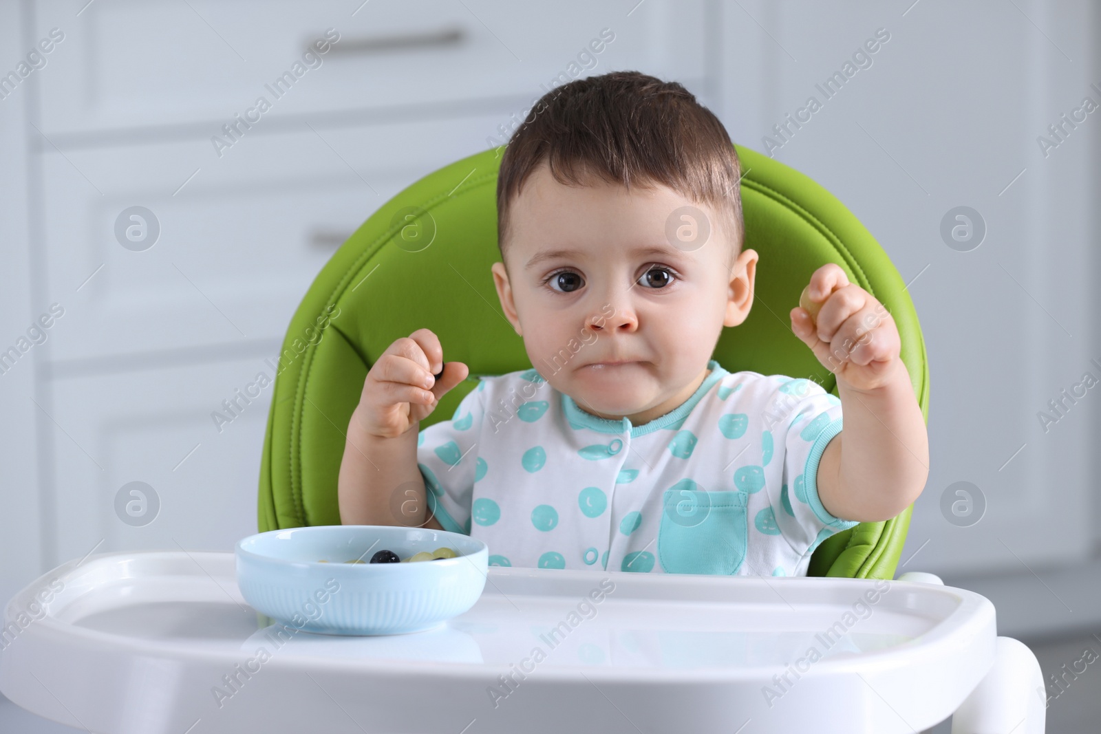 Photo of Cute little baby eating healthy food in high chair at home