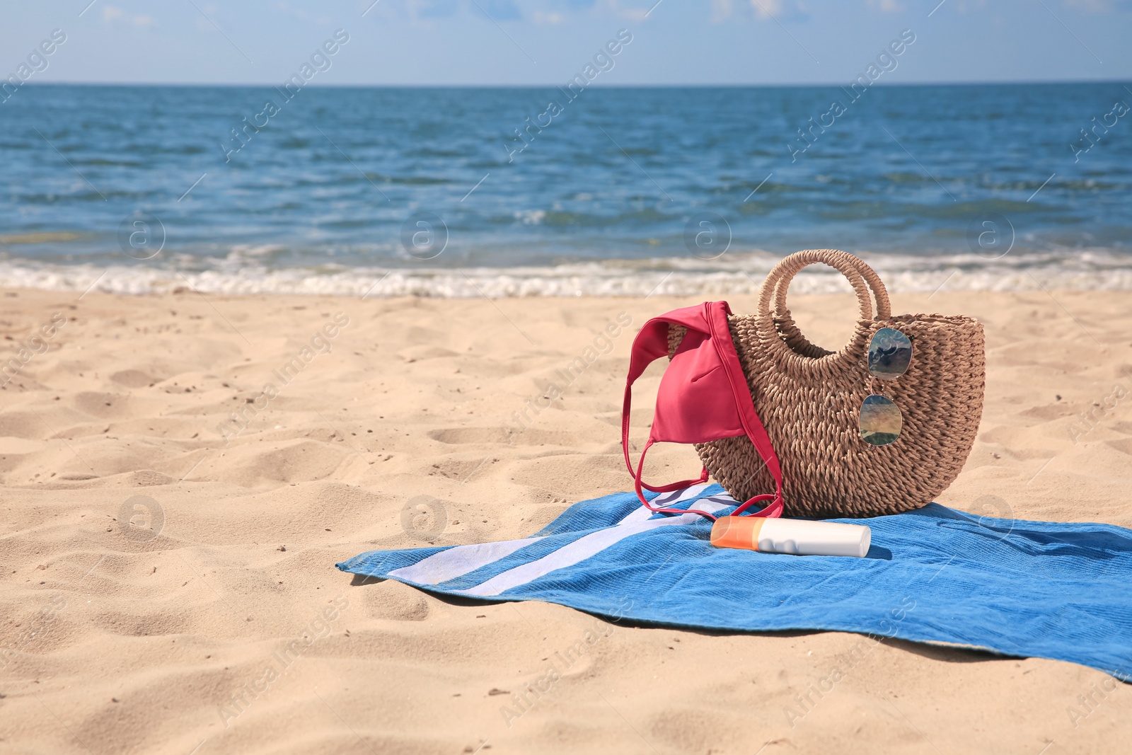 Photo of Blue striped beach towel with bag, swimsuit and accessories on sandy seashore, space for text