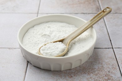 Baking powder in bowl and spoon on light tiled table, closeup