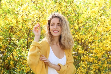 Attractive young woman posing near blossoming bush on sunny spring day