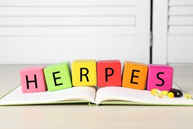 Photo of Word Herpes made of colorful cubes, open book and pills on beige table