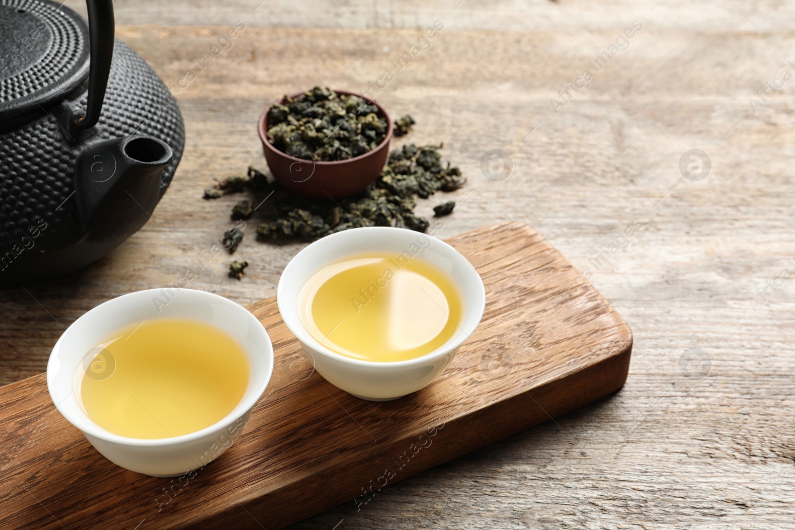 Photo of Cups and teapot of Tie Guan Yin oolong on wooden table. Space for text