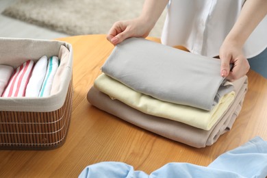 Photo of Woman folding clothes at wooden table indoors, closeup