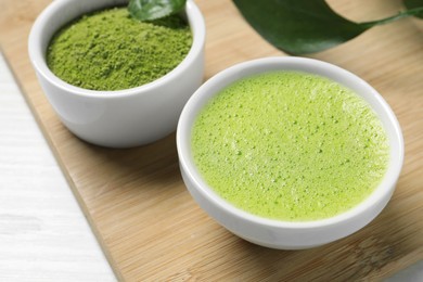 Cup of fresh matcha tea and green powder on wooden board, closeup