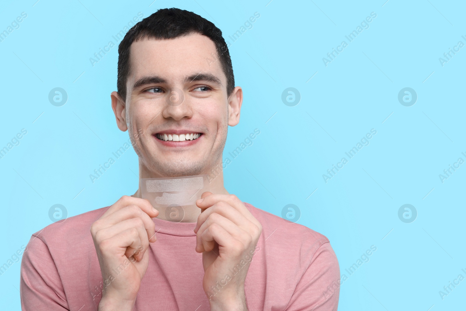 Photo of Young man with whitening strips on light blue background. Space for text