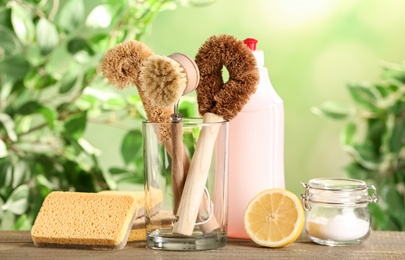 Different cleaning supplies for dish washing on wooden table against blurred background