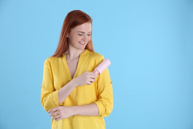 Photo of Young woman cleaning clothes with lint roller on light blue background, space for text