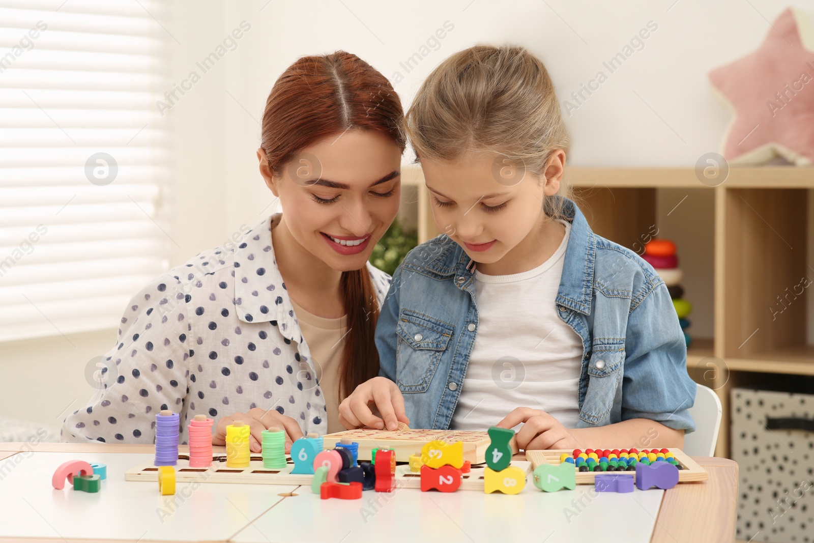 Photo of Happy mother and daughter playing with different math game kits at desk in room. Study mathematics with pleasure