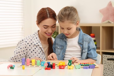 Photo of Happy mother and daughter playing with different math game kits at desk in room. Study mathematics with pleasure