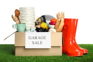 Box with sign Garage Sale and different stuff on green grass against white background