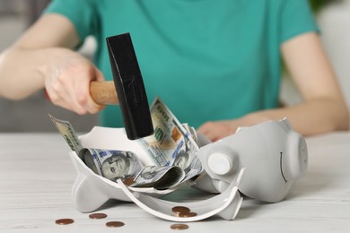 Financial savings. Woman breaking piggy bank with hammer at table indoors, closeup