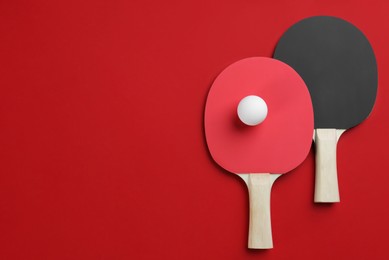 Photo of Ping pong rackets and ball on red background, flat lay. Space for text