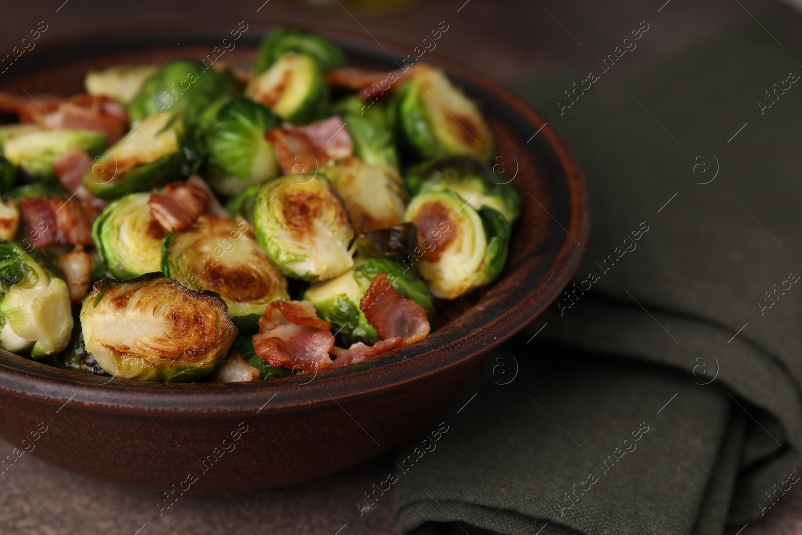 Photo of Delicious roasted Brussels sprouts and bacon in bowl on brown table, closeup