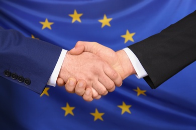 Men shaking hands against flag of European Union, closeup. International relationships