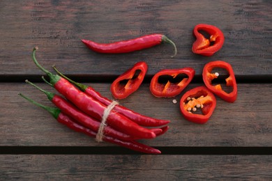 Whole and cut red chili peppers on wooden table, flat lay