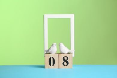 Photo of Decorative ceramic birds and wooden block calendar on table against color background. International Women's Day