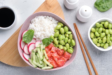 Photo of Poke bowl with salmon, edamame beans and vegetables on light grey table, flat lay