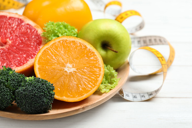 Photo of Fruits, vegetables and measuring tape on white wooden background, closeup. Visiting nutritionist