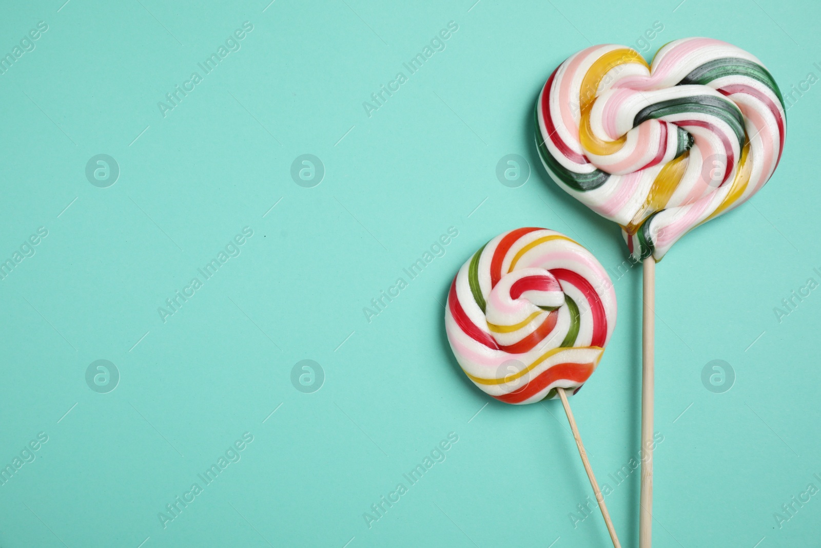 Photo of Sticks with different colorful lollipops on turquoise background, flat lay. Space for text