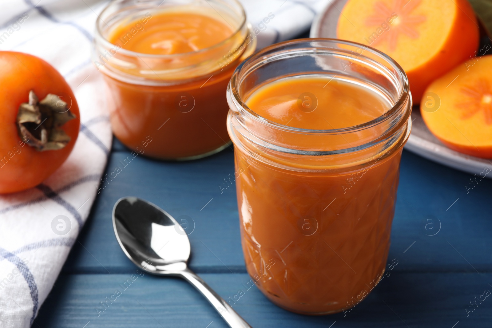 Photo of Delicious persimmon jam in glass jars served on blue wooden table, closeup