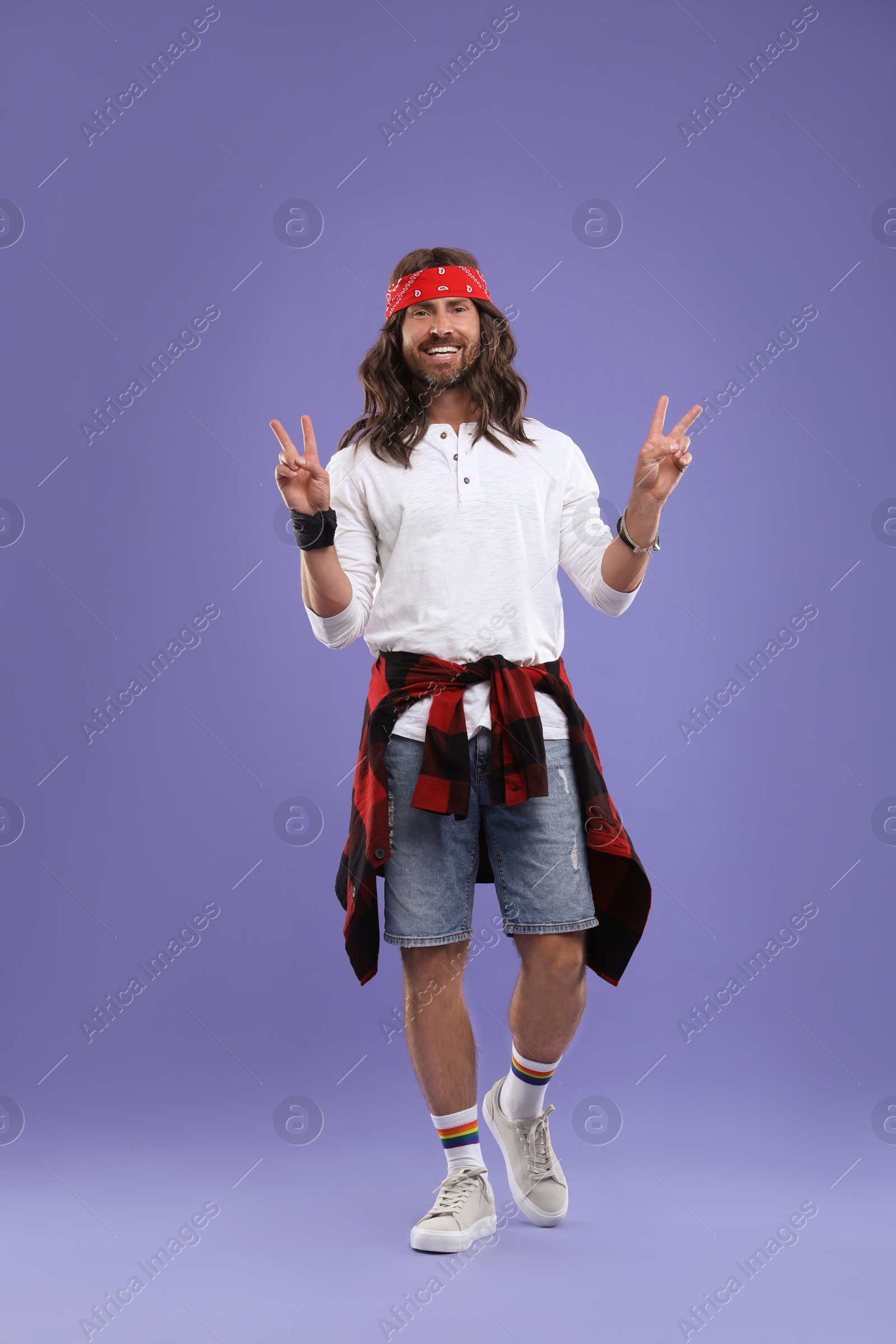 Photo of Stylish hippie man showing V-sign on violet background