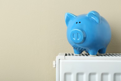 Piggy bank on heating radiator against beige background, space for text