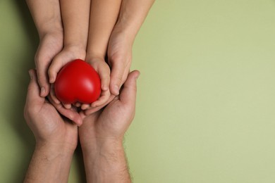 Photo of Parents and child holding red decorative heart on light green background, top view. Space for text